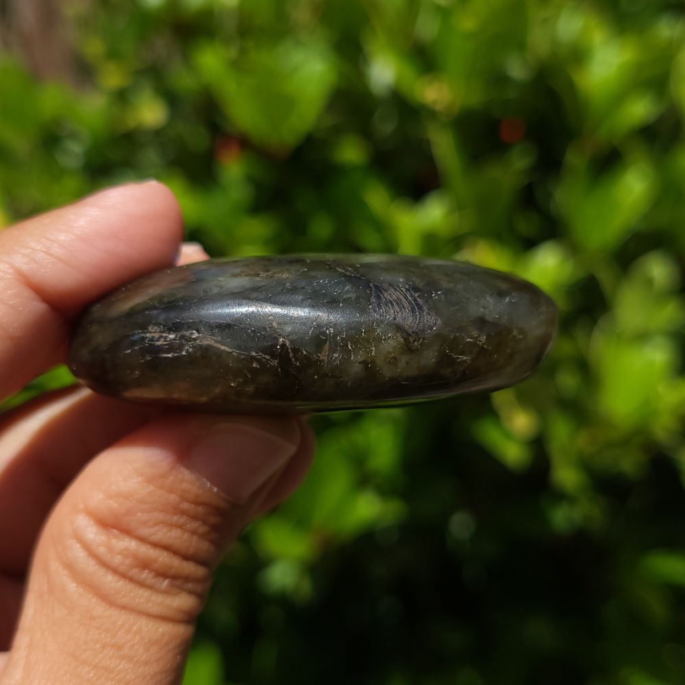 Hand holding a labradorite palm stone against a blurred green background