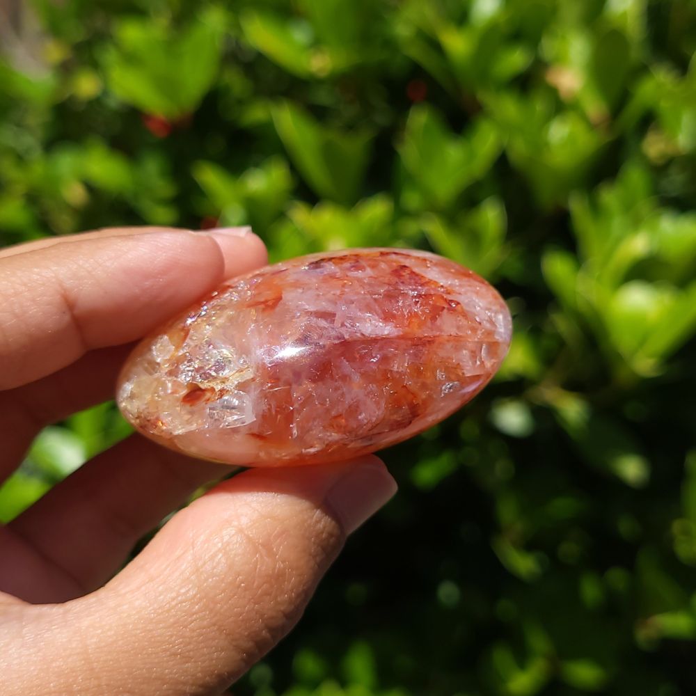 Hand holding a hematoid quartz crystal stone with a green blurred background