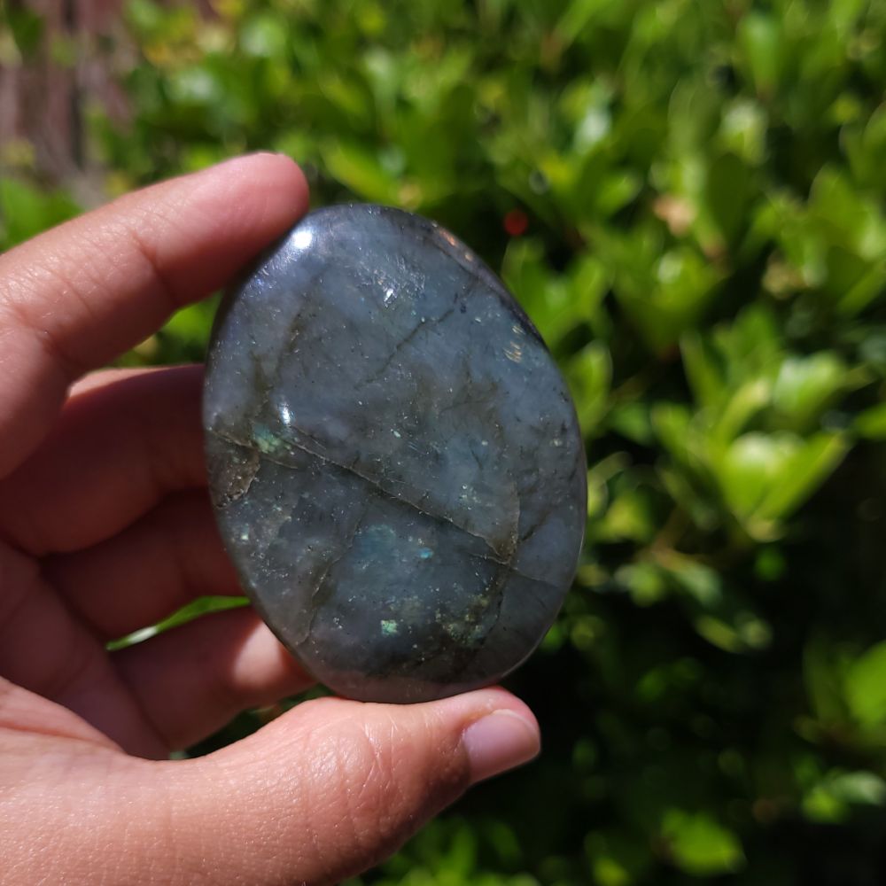 Hand holding a labradorite stone with a blurred green outdoor background