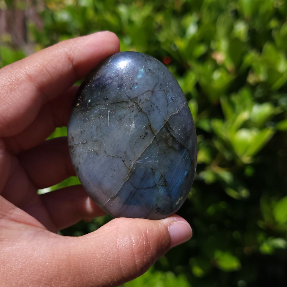 Hand holding a labradorite stone with a blurred green background
