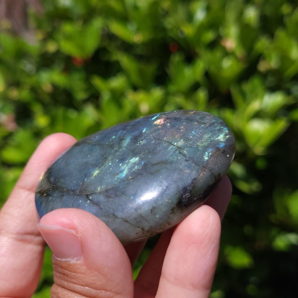 Hand holding a labradorite stone with a blurred green background