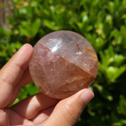 Hand holding a fire quartz palm stone with a green outdoor background