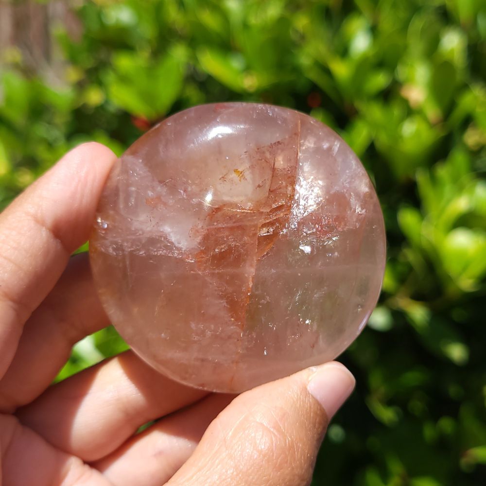 Hand holding a fire quartz palm stone with a blurred green outdoor background