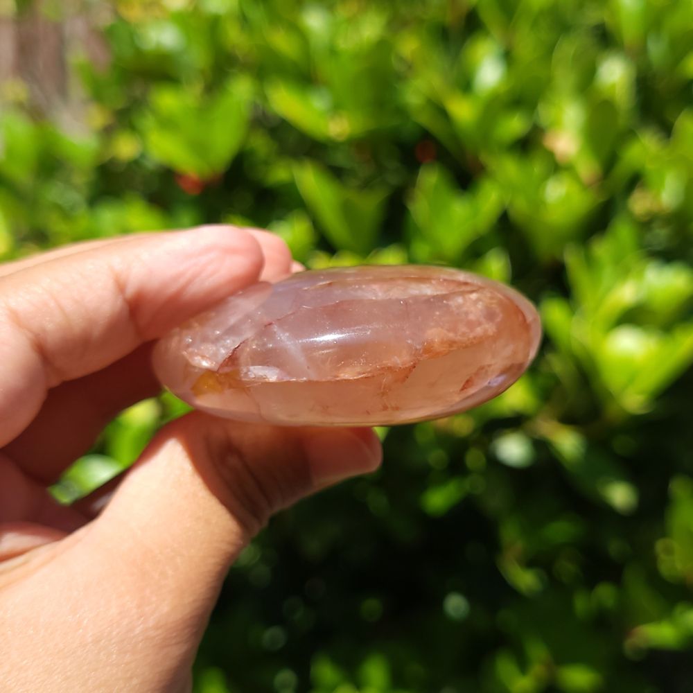 Hand holding a hematoid quartz palm stone with a green blurred background