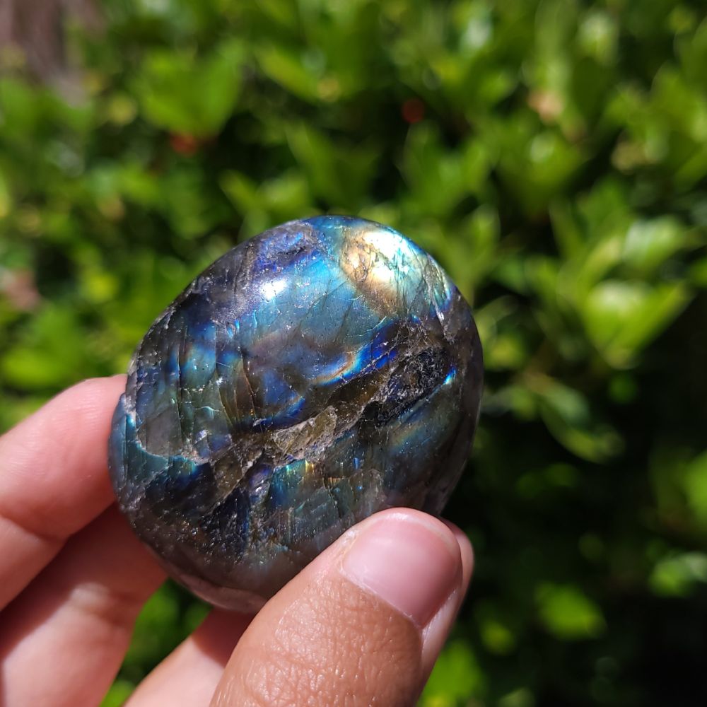 Labradorite stone held in a hand with a blurred green background