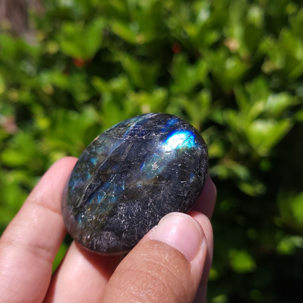 Person holding a labradorite stone with a reflective surface against a green outdoor background