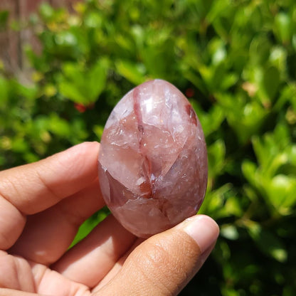 Hand holding a fire quartz palm stone against a green leafy background