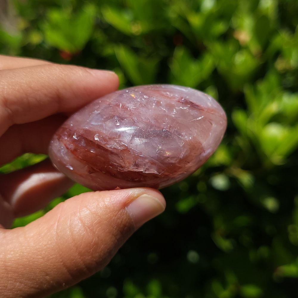 Hand holding a hematoid quartz palm stone with a blurred green background
