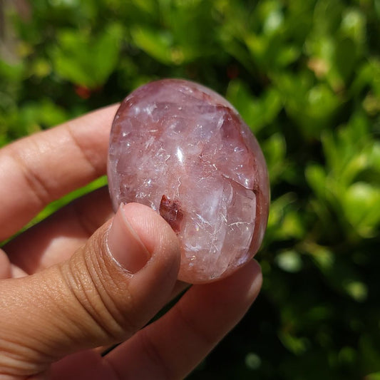 Hand holding a fire quartz palm stone against a green leafy background