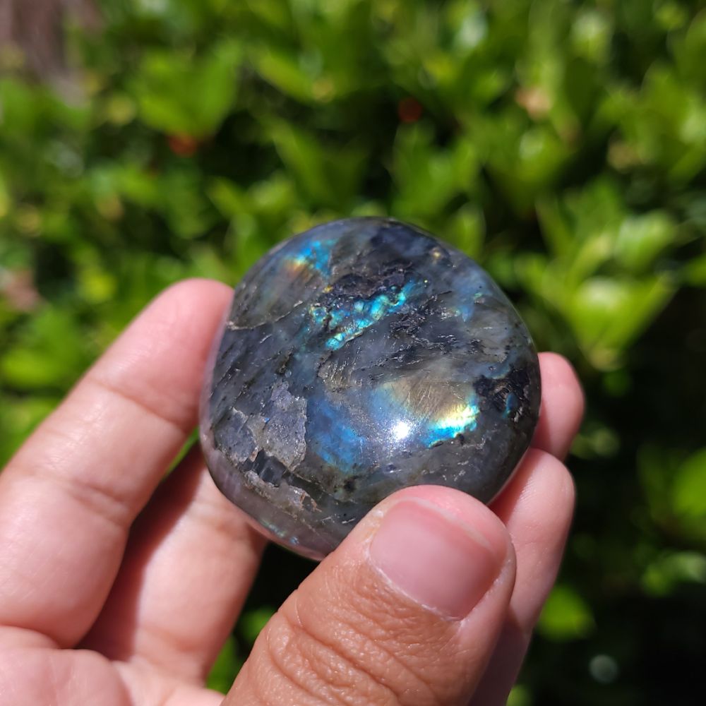 Person holding a labradorite stone with a reflective surface against a blurred green background