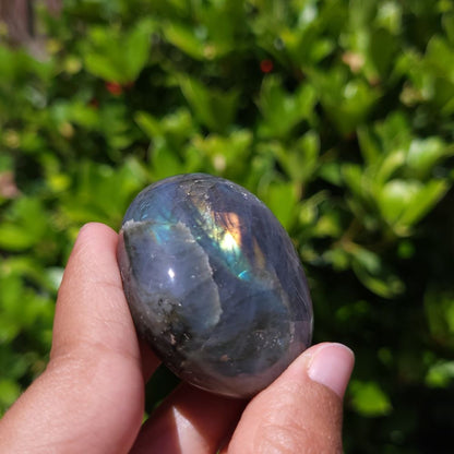 Person holding a labradorite stone with a blurred green outdoor background