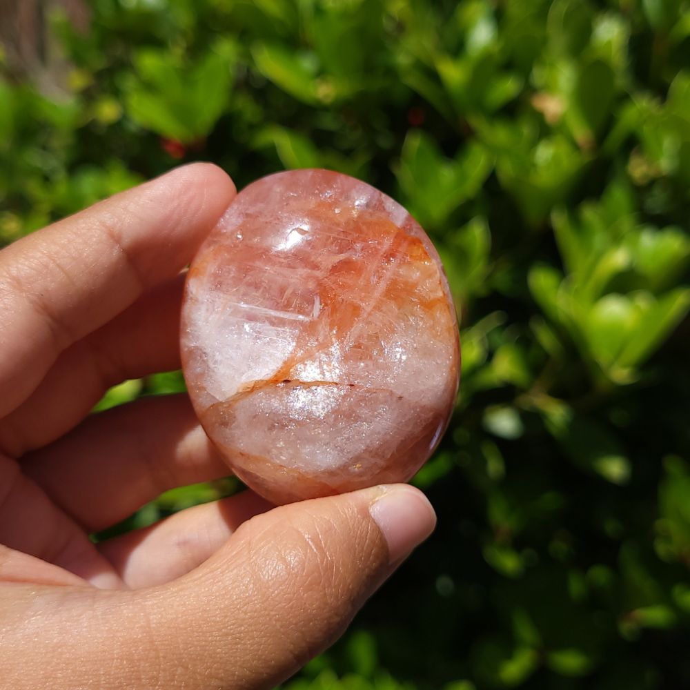Hand holding a fire quartz palm stone with a green leafy background