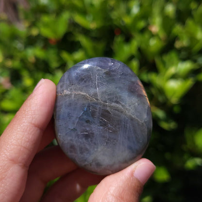 Hand holding a labradorite palm stone with a blurred green background
