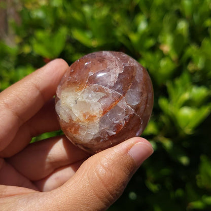 Hand holding a polished Fire Quartz palm stone with a natural green background