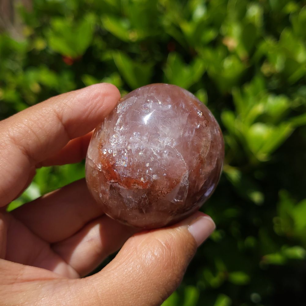 Hand holding a polished Fire Quartz palm stone with a green blurred background