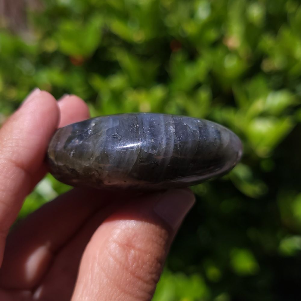 Hand holding a labradorite palm stone against a blurred green background