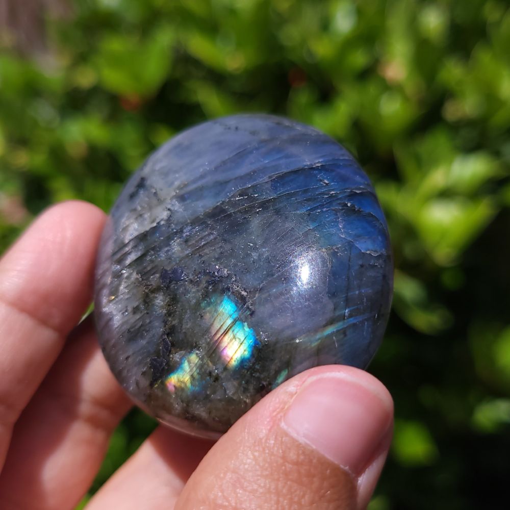 Person holding a Labradorite stone with a reflective surface against a blurred green background