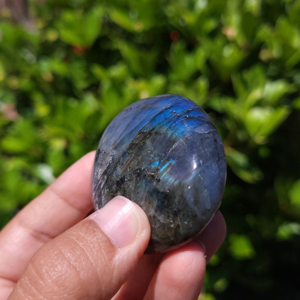 Hand holding a labradorite stone with a blurred green background