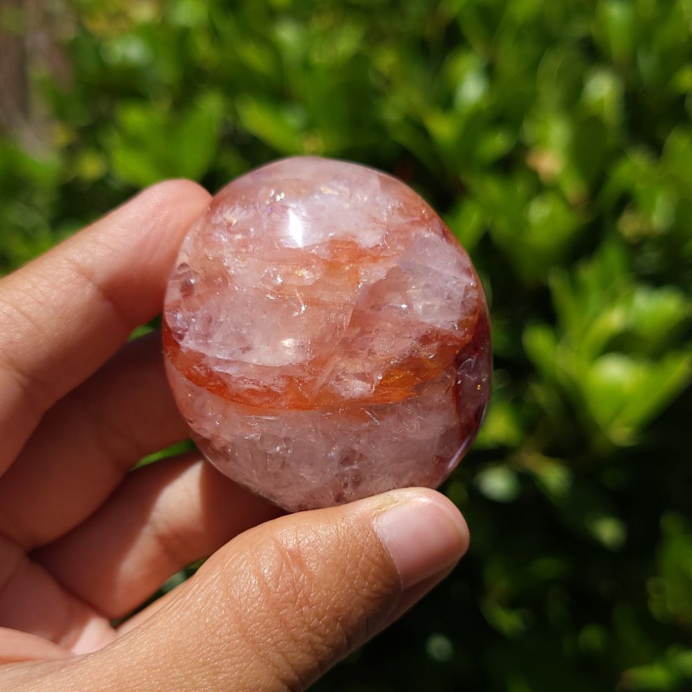 Hand holding a Hematoid Quartz palm stone with a blurred green background