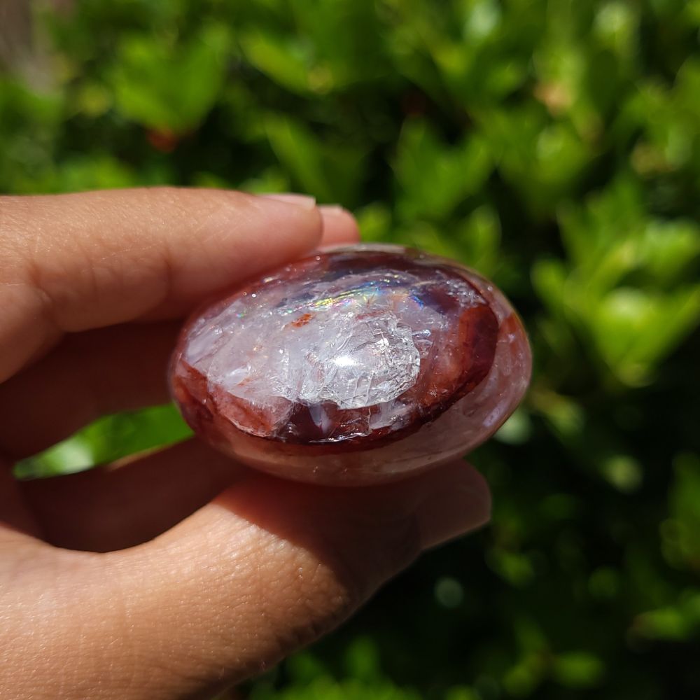 Hand holding a polished Hematoid Quartz palm stone with a green outdoor background