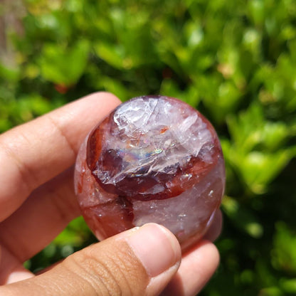 Hand holding a Hematoid Quartz palm stone with a green blurred background