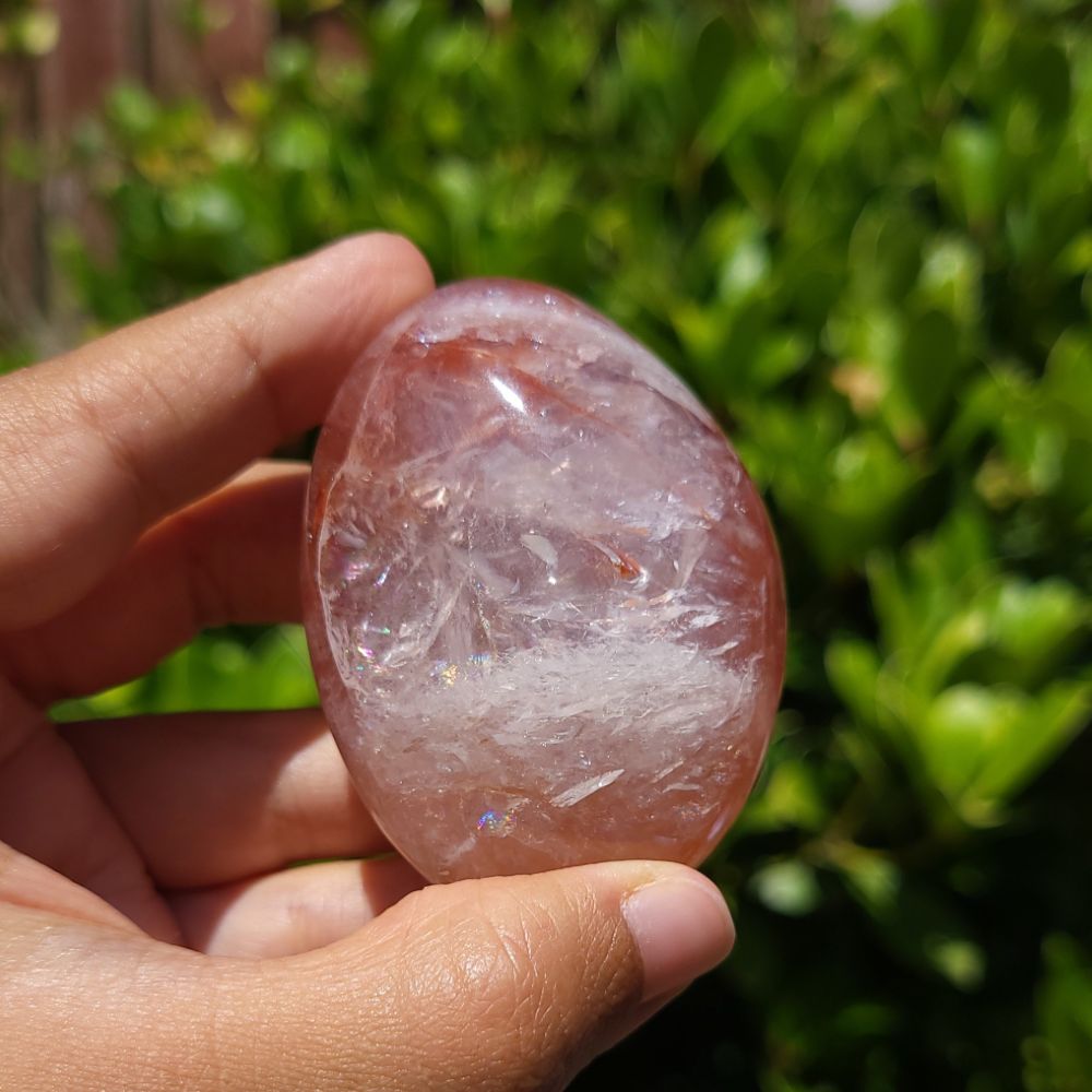Hand holding a Fire Quartz palm stone with a blurred green background