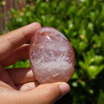Hand holding a Fire Quartz palm stone with a blurred green background