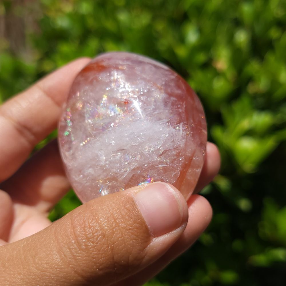 Hand holding a Fire Quartz palm stone with a blurred green background