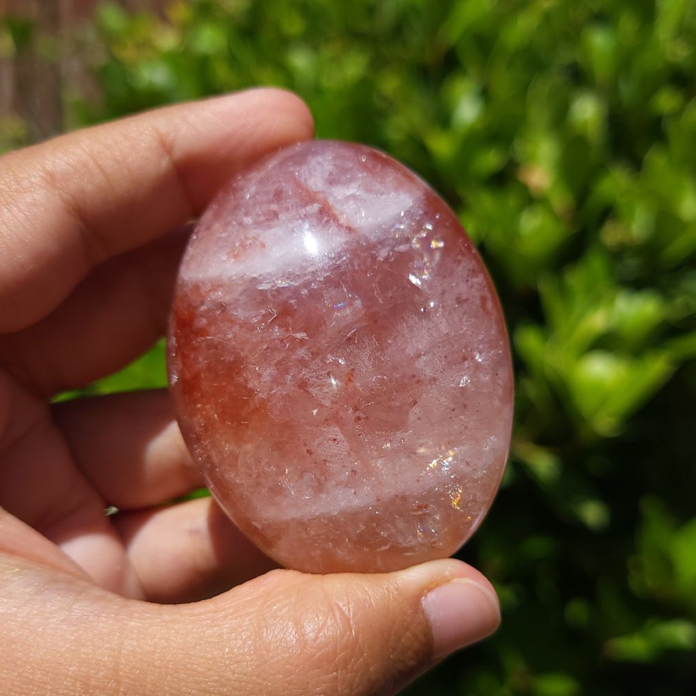 Hand holding a Fire Quartz palm stone with a blurred green background