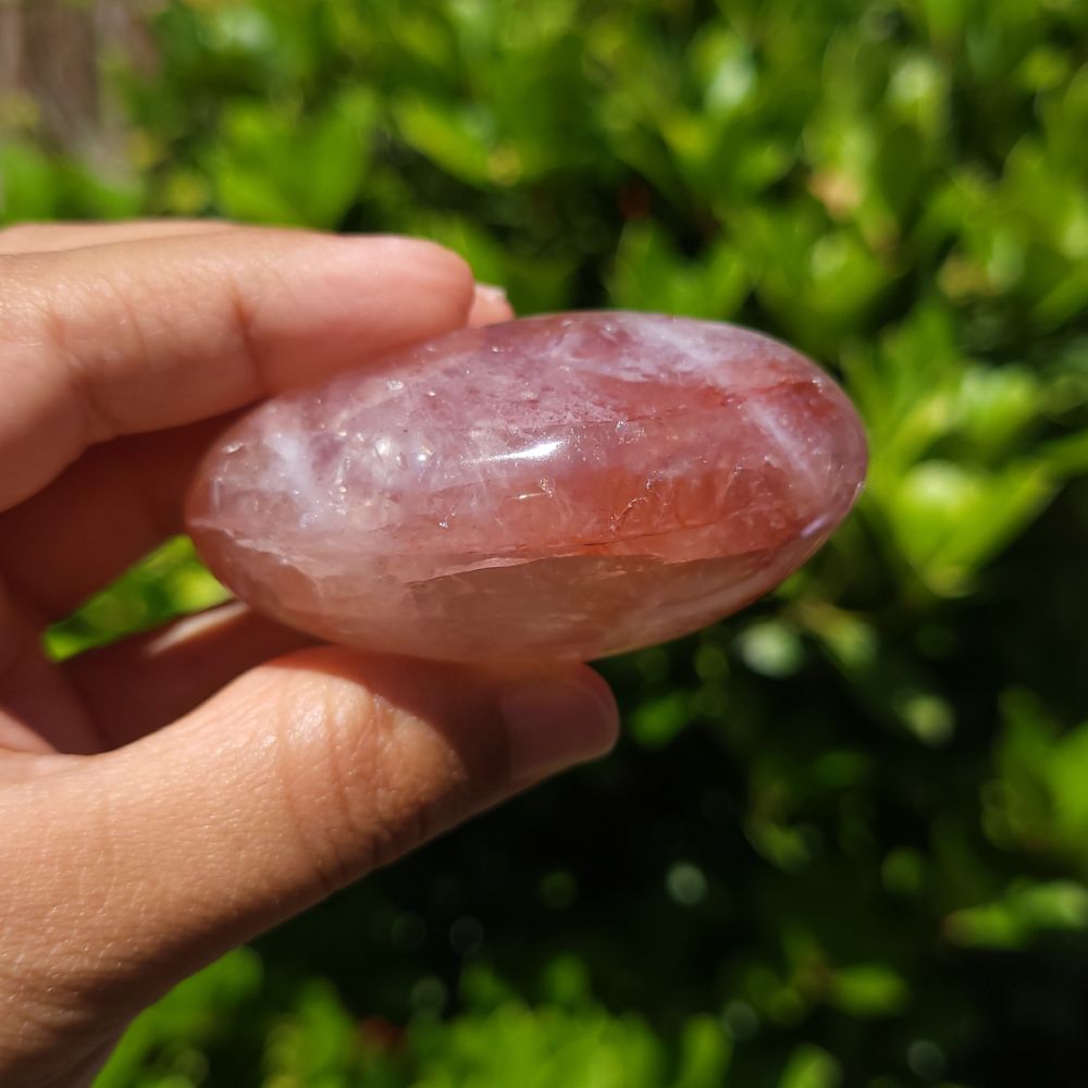 Hand holding a Fire Quartz palm stone with a green leafy background