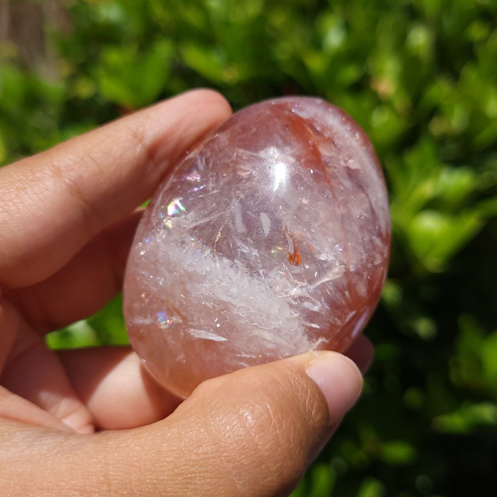 Hand holding a Fire Quartz palm stone with a green blurred background