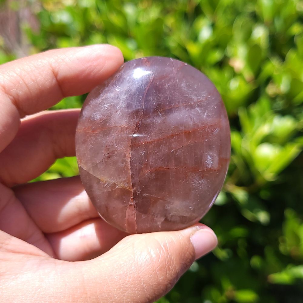Hand holding a Fire Quartz palm stone with a green outdoor background