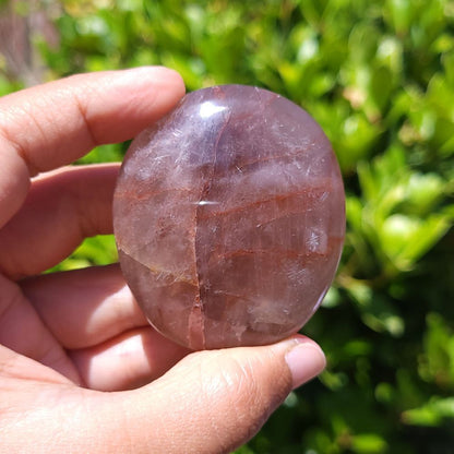 Hand holding a Fire Quartz palm stone with a green outdoor background