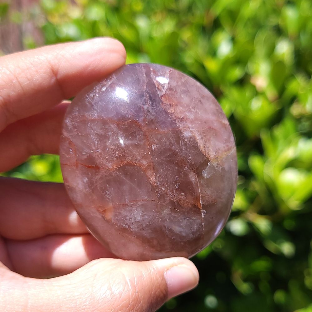 Hand holding a Fire Quartz palm stone with a blurred green background