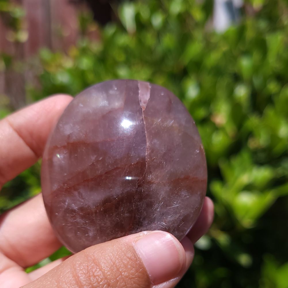 Hand holding a Fire Quartz palm stone with a blurred green background
