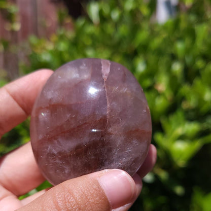 Hand holding a Fire Quartz palm stone with a blurred green background
