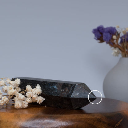 Arfvedsonite tower crystal on a wooden surface with white and purple flowers in the background
