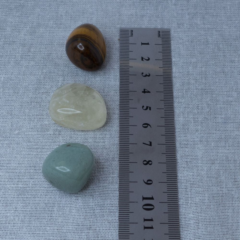 Three stones of different colors on a textured surface with a ruler for scale.