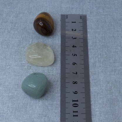 Three stones of different colors on a textured surface with a ruler for scale.