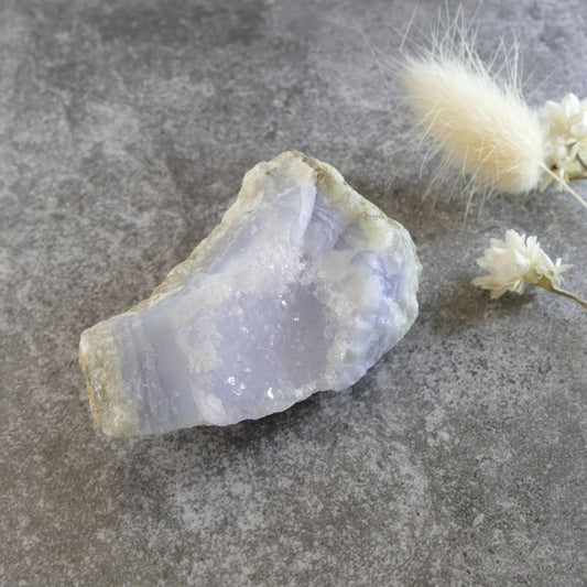 Natural blue lace agate stone, approximately 6x3.2x2.4cm, showing its signature light blue and white layers, accented with clear quartz crystals. Image for crystal collectors and those interested in metaphysical properties.