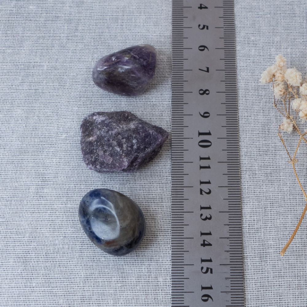 Three purple stones on a textured surface with a ruler for scale.