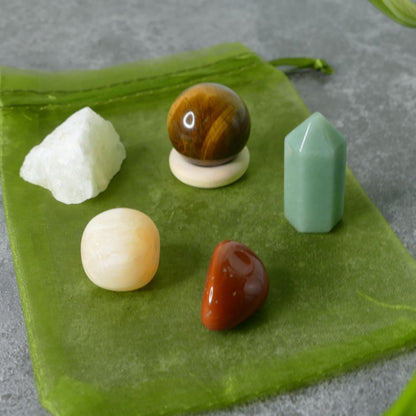 Set of raw lemon quartz, tiger's eye sphere, green aventurine mini tower, orange calcite and red jasper tumbled stones  on a green fabric background