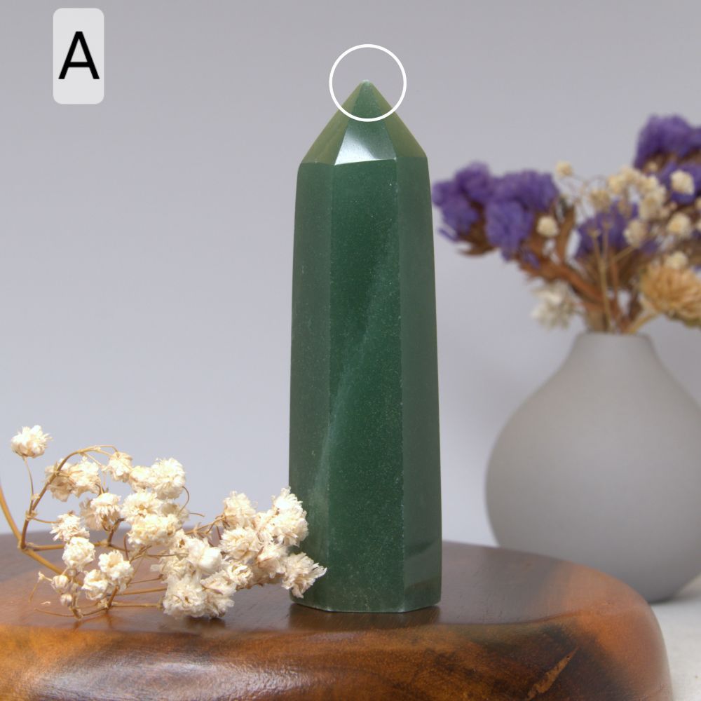 Green aventurine crystal tower on a wooden surface with flowers in the background