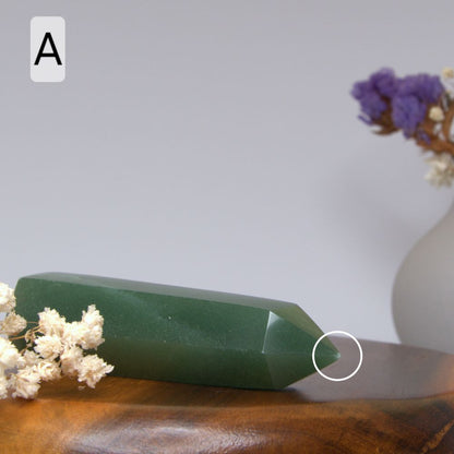 Green aventurine crystal on a wooden surface with flowers and a vase in the background