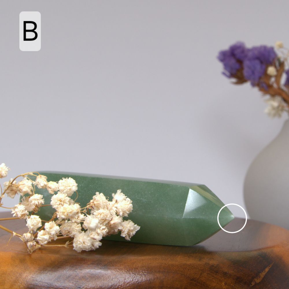 Green crystal on a wooden surface with white flowers and a blurred vase in the background