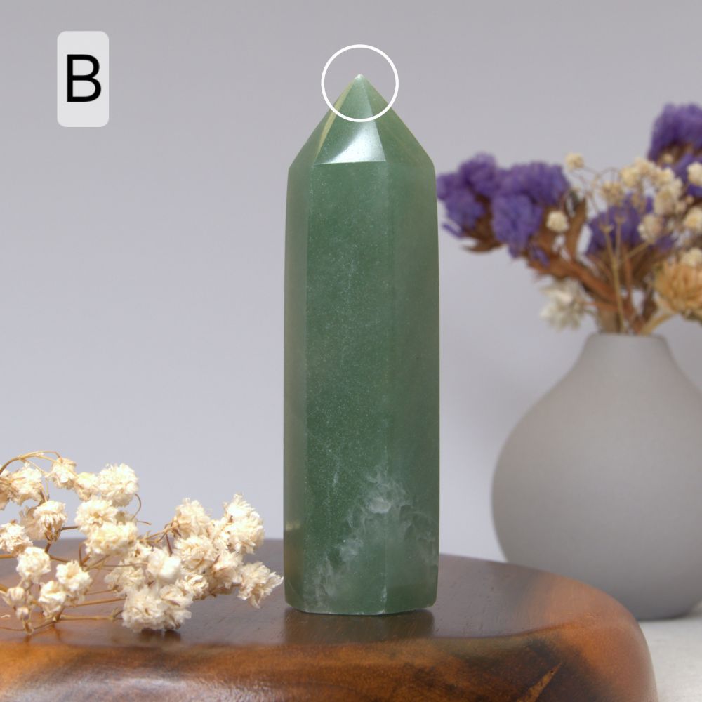 Green aventurine crystal on a wooden surface with flowers in the background