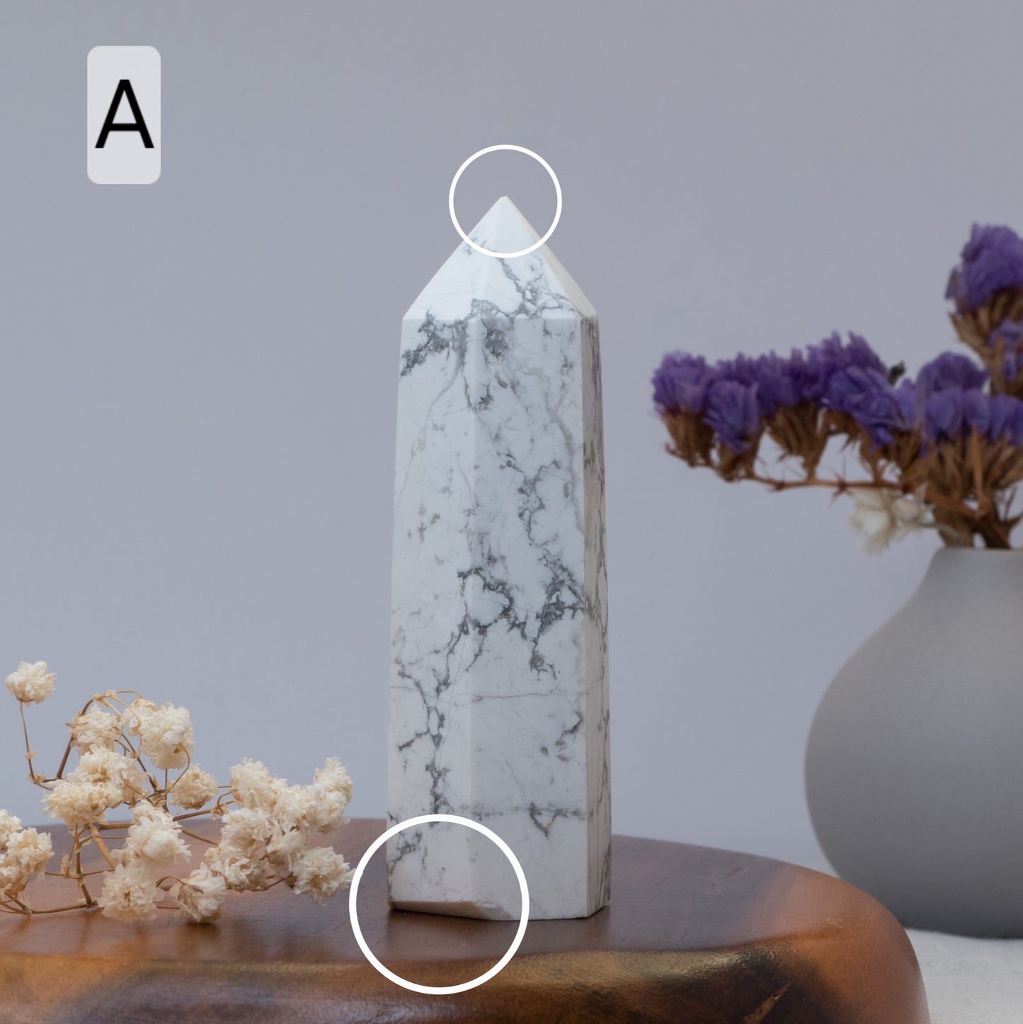 Howlite tower on a wooden surface with a vase of purple flowers in the background.
