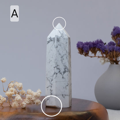 Howlite tower on a wooden surface with a vase of purple flowers in the background.