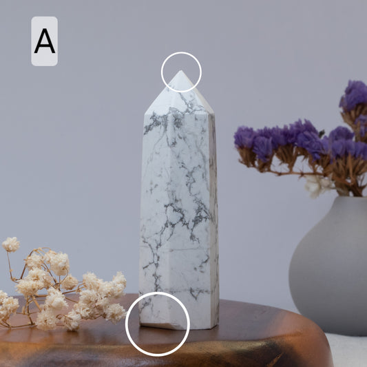 Howlite tower on a wooden surface with a vase of purple flowers in the background.