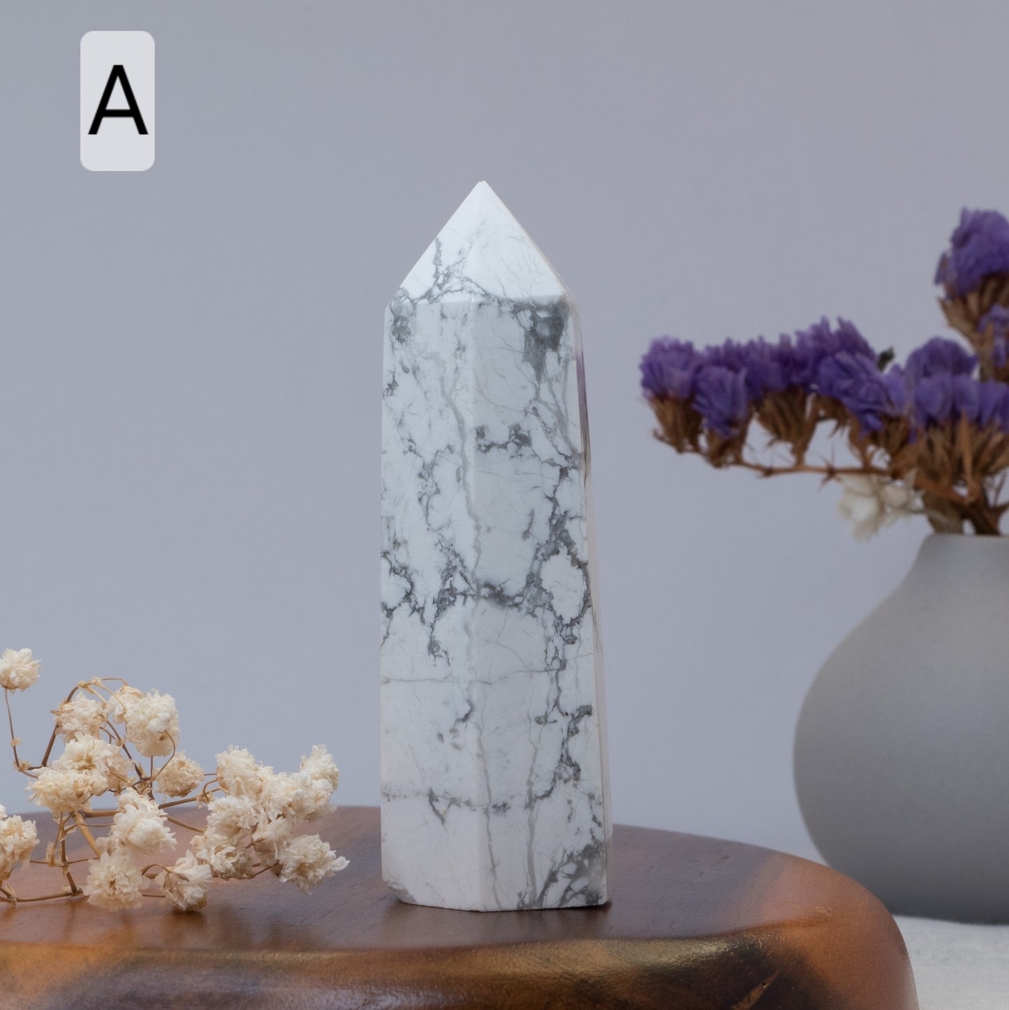 Howlite tower on a wooden surface with a vase of purple flowers in the background